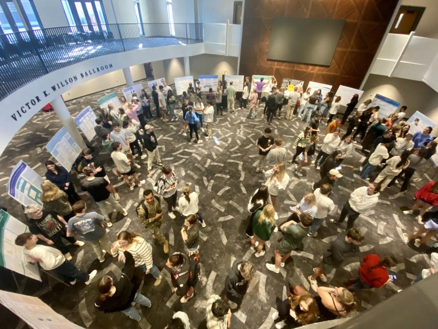 overhead view of poster session. 24 easels arranged in large circle and large crowd observing 