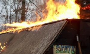 The sign warns skaters to skate at their own risk as flames engulf the ramp. v